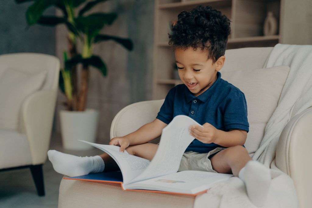 Happy mixed race little kid reading at home.