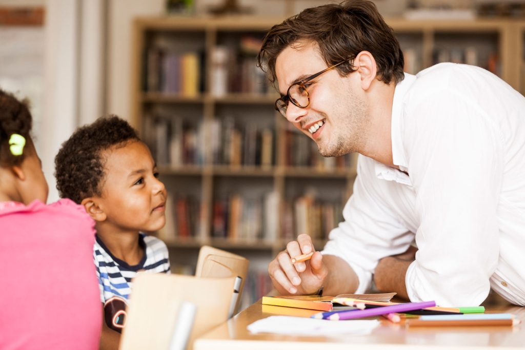 Smiling male teacher teaching 2 kids.