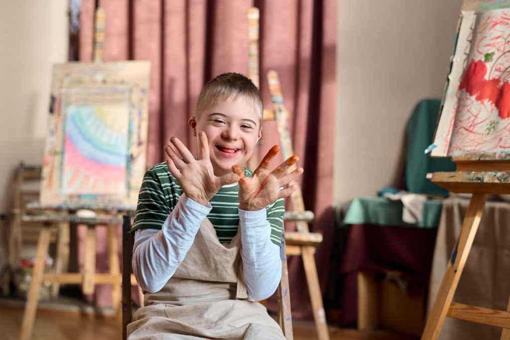 Boy with down syndrome happy with paints on his hands.