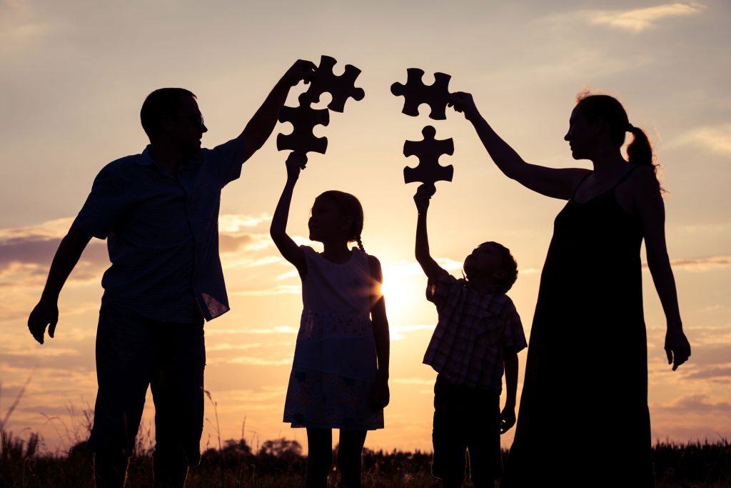 Family holding jigsaw puzzle at sunset.