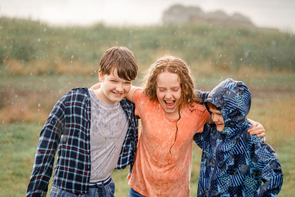 Children smiling and hugging each other in the rain.